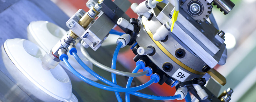 Närbild på en industriell robotarm med vakuumsugkoppar och blå pneumatiska slangar som hanterar formsprutade plastdetaljer. Utrustningen är märkt med siffran 45.