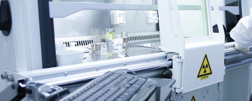 Interior of a sterile laboratory or cleanroom with a radiation symbol on equipment. The image shows a workstation with metal instruments, liquids, and a keyboard in the foreground.