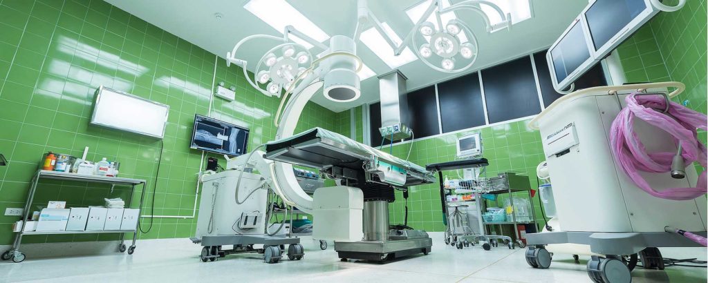 Operating room with advanced medical technology equipment and green-tiled walls.