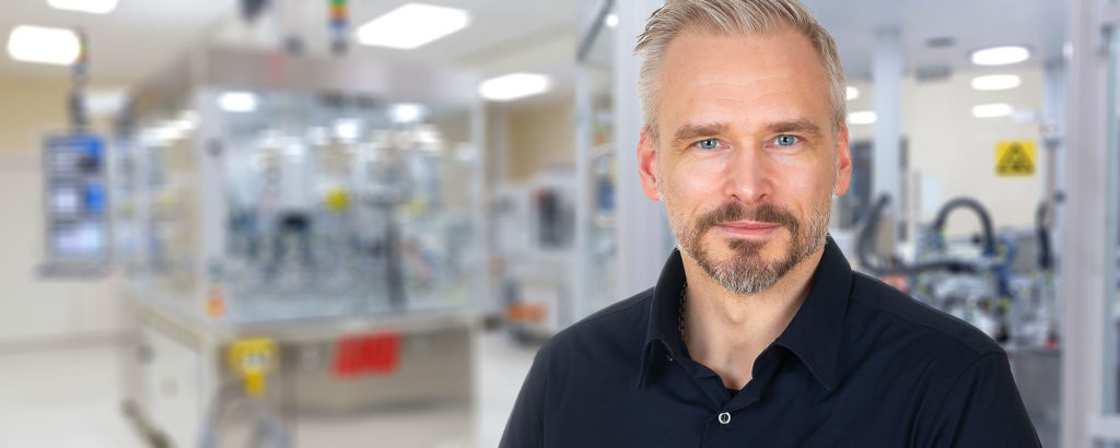 Robert Rudensjö i svart skjorta står i fokus med oskarp bakgrund av en medicinteknisk produktionsmiljö.
