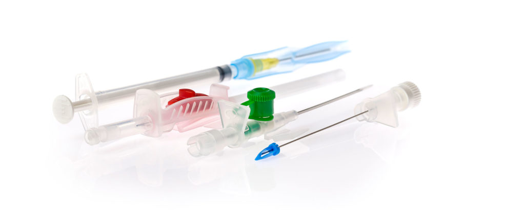 Close-up of various single-use medical instruments, including cannulas and plastic components in different colors, placed on a white background.