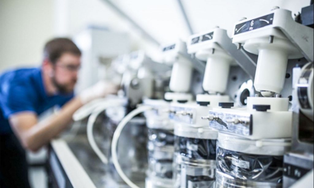 Närbild av medicinteknisk utrustning i ett laboratorium, med en tekniker i bakgrunden som arbetar med test- eller kalibreringsutrustning.