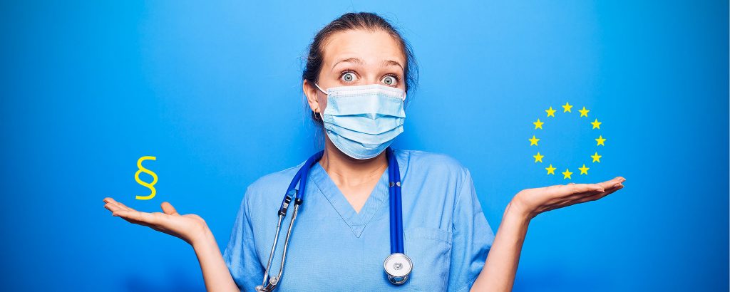 Sjukvårdspersonal i blå kläder och munskydd ser frågande ut med armarna utsträckta åt sidorna. I ena handen visas ett paragraftecken (§), i den andra EU:s stjärnring. Bilden symboliserar osäkerhet kring regelverk inom EU:s sjukvård eller medicinteknik.