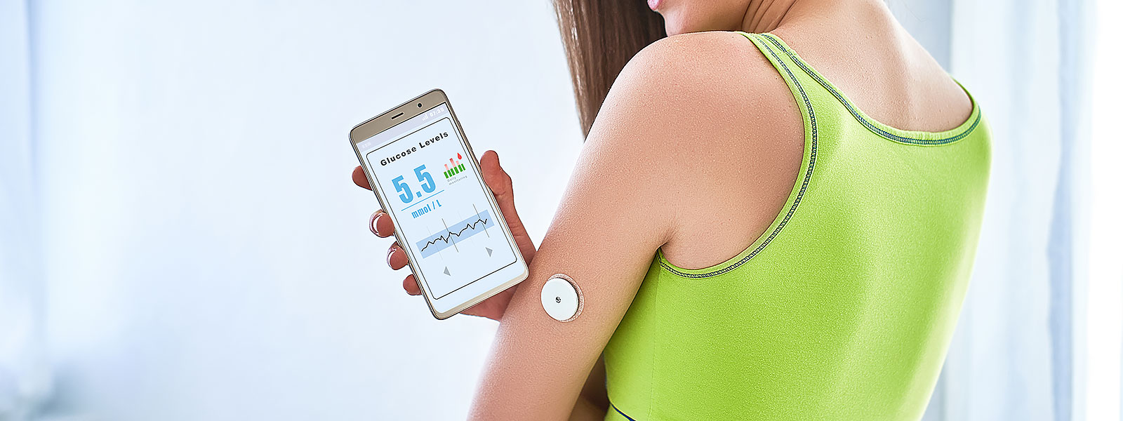 Kvinna med glukossensor på överarmen läser sina blodsockervärden i en mobilapp. Skärmen visar 5,5 mmol/L.
