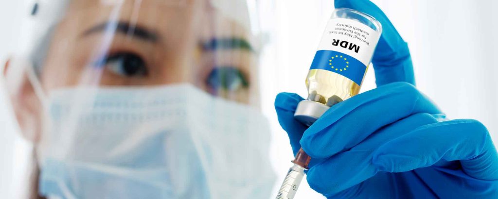 Närbild på vårdpersonal med munskydd och visir som hanterar en MDR-märkt injektionsflaska med spruta.